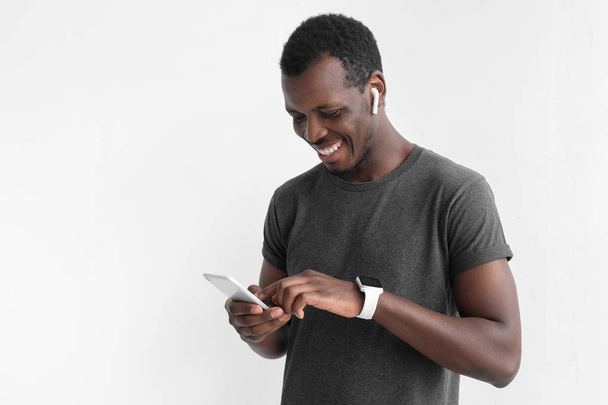 Young attractive african american dark skin man looking at smartphone while texting, using mobile phone, isolated on gray background - Foto, Imagem