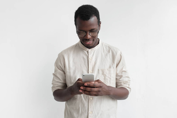 Young african american man in pale shirt, isolated on gray background, texting or browsing with happy relaxed smile - Фото, зображення