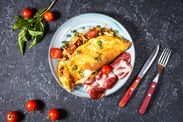 Omelet met tomaten, champignons en spek. Ontbijt op stenen achtergrond. Gezonde voeding. Bovenaanzicht. Plat leggen - Foto, afbeelding