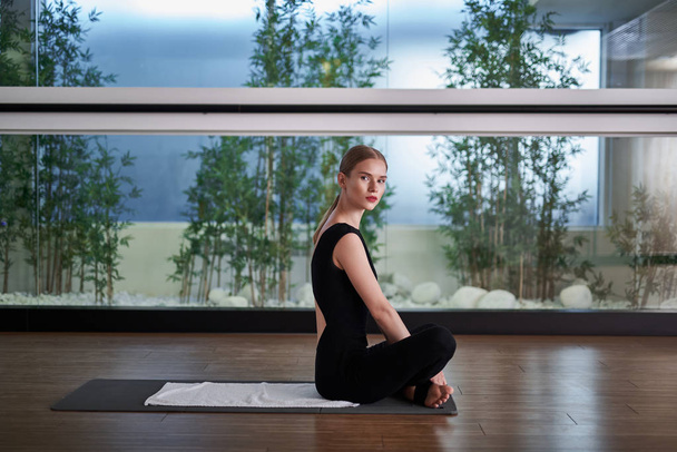 Молода жінка сидить на килимку під час практики йоги
 - Фото, зображення