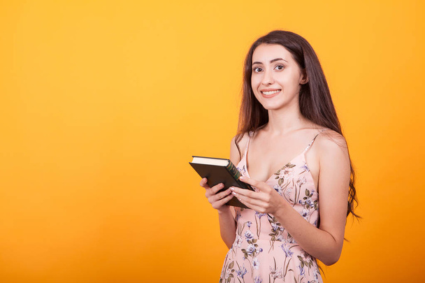Magnifique jeune femme tient un livre en studio sur fond jaune
 - Photo, image