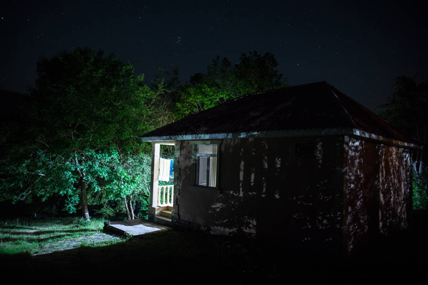 Ночной горный пейзаж постройки в лесу ночью с луной или винтажным загородным домом ночью с облаками и звездами. Летняя ночь. Фотография сделана с большой экспозицией
 - Фото, изображение