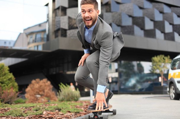 Confident young businessman in business suit on longboard hurrying to his office, on the street in the city - Foto, Imagem