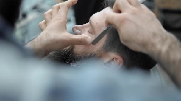 Barber holí muži s dlouhým vousem s rovnou razor blade s kadeřnictví nebo holičství. Mans střih a holení v kadeřnictví, holičství a holení salonu. - Záběry, video