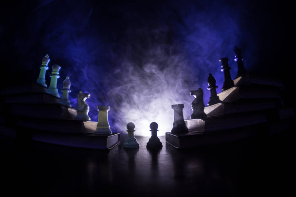 Ιεραρχία επιχειρήσεων. Στρατηγική αντίληψη με τα κομμάτια του σκακιού. Σκάκι στέκεται σε μια πυραμίδα των βιβλίων με το βασιλιά στην κορυφή. Σκούρο ομιχλώδες φόντο με τονισμένο φως. Χώρο αντίγραφο. - Φωτογραφία, εικόνα