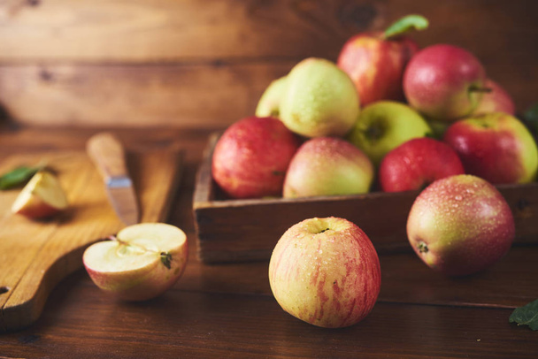 Friss érett alma-fa dobozban, kést, és a fele alma vágódeszka, fából készült barna háttér felett - Fotó, kép