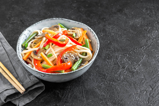 Stir fry with udon noodles, mushrooms and vegetables in bowl. Asian vegan vegetarian food, meal, stir fry over black background, copy space. - Fotó, kép