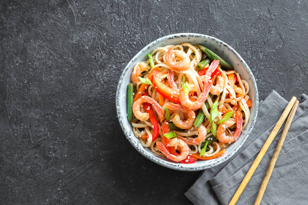 Stir fry with udon noodles, shrimps (prawns) and vegetables. Asian healthy food, meal, stir fry in bowl over black background, copy space. - Fotografie, Obrázek