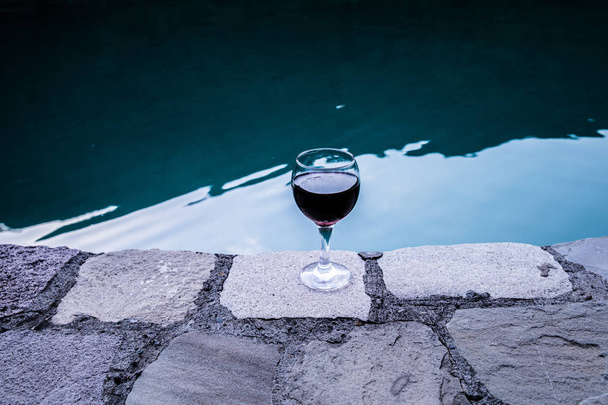 Drink in hoog glas in zwembad. Verfrissing op zomerdag. Paarse juice cocktail of vine. Berg bos achtergrond. Selectieve aandacht - Foto, afbeelding