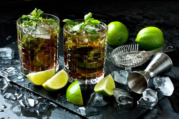 Two glasses of Cuba libre  cocktail with fresh lime and mint on  black tray, holidays party concept.  - Photo, image