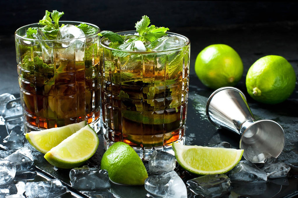 Cuba Libre or iced tea cocktail with strong alcohol, cola, lime and ice, two glass, dark background  with copy space - Zdjęcie, obraz