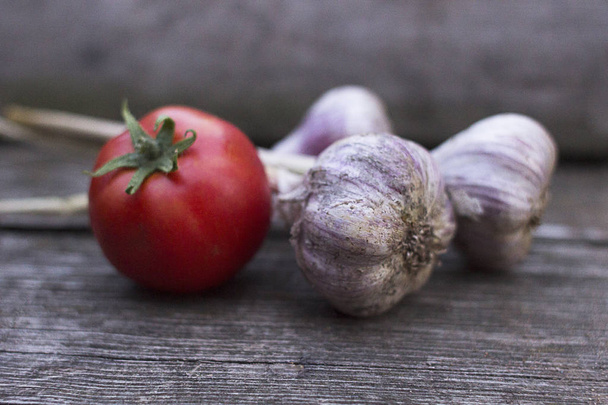 Ripe red tomato and garlic on an old wooden background. New crop - Zdjęcie, obraz