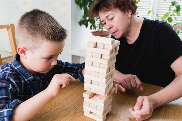 Woman and kid are playing jenga game. Trying to keep balance of tower from wooden blocks. Family leasure time. Concept of risk and stratery in business and construction. - Фото, изображение