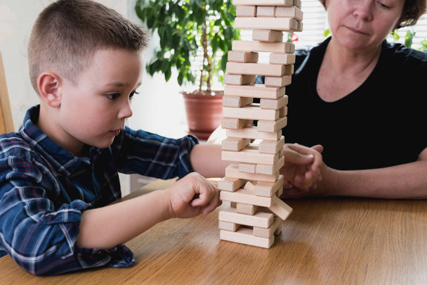 Woman and kid are playing jenga game. Trying to keep balance of tower from wooden blocks. Family leasure time. Concept of risk and stratery in business and construction. - Фото, изображение