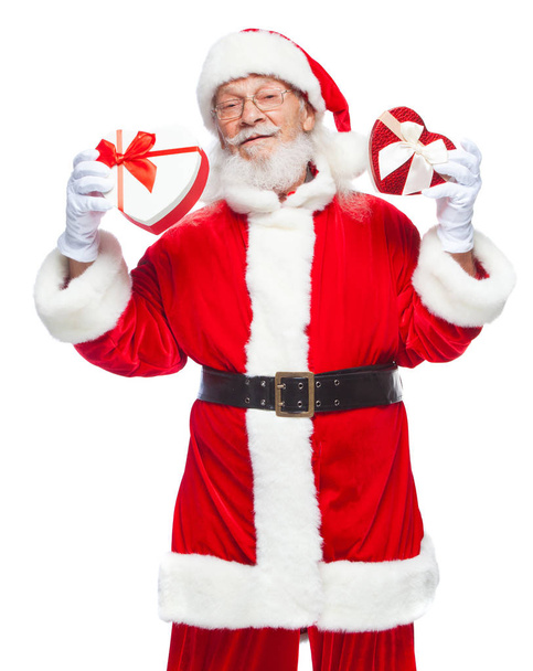 Vánoce. Usmívající se Santa Claus v bílých rukavicích drží dva dárkové krabičky ve tvaru srdce červené a bílé se stuhou. Koncept štědré dary. Izolované na bílém pozadí. - Fotografie, Obrázek