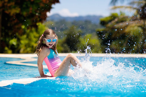 A gyerek a medencében játszik. Nyári vakáció gyerekekkel. Kislány ugrik a vízbe az egzotikus nyaralás során a trópusi szigeten üdülőhelyen. A gyerekek úsznak. Aktív szabadtéri sport óvodások számára. - Fotó, kép