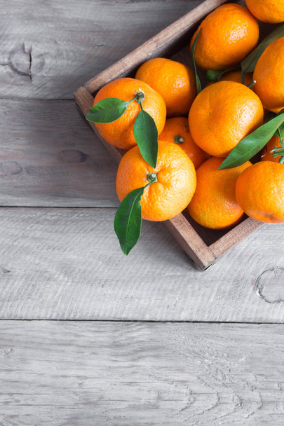Mandarynki (pomarańcze, klementynki, owoce cytrusowe) z zielonymi liśćmi na drewnianym tle z przestrzenią do kopiowania - Zdjęcie, obraz