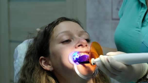 Επίσκεψη στον οδοντίατρο, η εγκατάσταση του συστήματος βραχίονα. Ο Βοηθός λάμπει με ένα λαμπτήρα υπεριώδους ακτινοβολίας οδοντιατρική πολυμερισμού για σταθεροποίηση του close-up αγκύλες. - Πλάνα, βίντεο