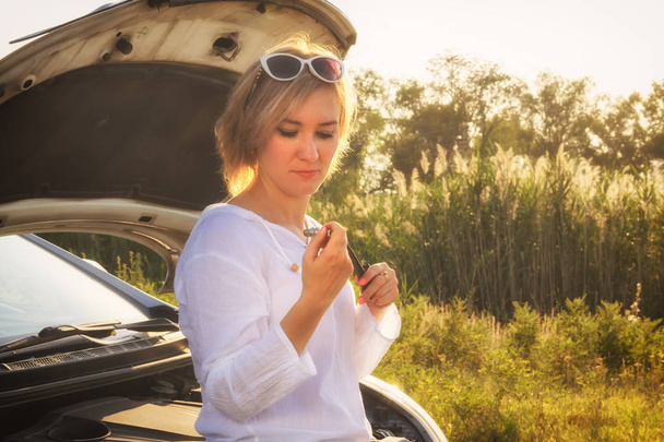 belle fille blonde est engagée dans la réparation d'une voiture sur une route de campagne et tient une clé et bougies d'allumage dans les rayons du coucher du soleil. Portrait
 - Photo, image