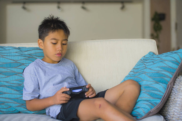 lifestyle portrait of Latin young kid 8 years old excited and happy playing video game online holding remote controller enjoying having fun on couch in child gaming emotion and addiction - Foto, Imagem