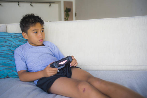 lifestyle portrait of Latin young kid 8 years old excited and happy playing video game online holding remote controller enjoying having fun on couch in child gaming emotion and addiction - Photo, Image