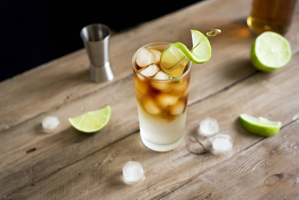 Dark and Stormy Rum Cocktail with Ginger Beer and Lime garnish. Glass of Dark and Stormy Cocktail drink on wooden table, copy space. - Photo, Image