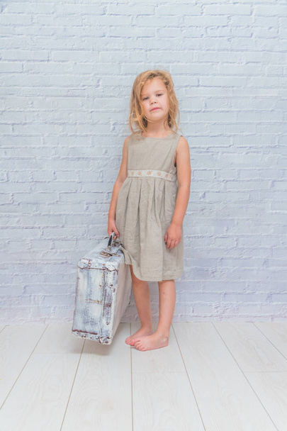 girl, baby in dress on white brick wall background with suitcase - Zdjęcie, obraz