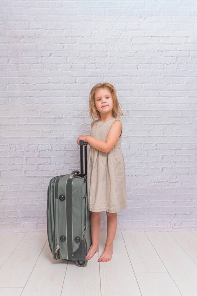 girl, baby in dress on white brick wall background with suitcase - Foto, Imagen