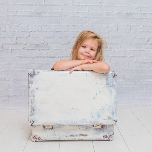 girl, baby in dress on white brick wall background with suitcase - Фото, зображення