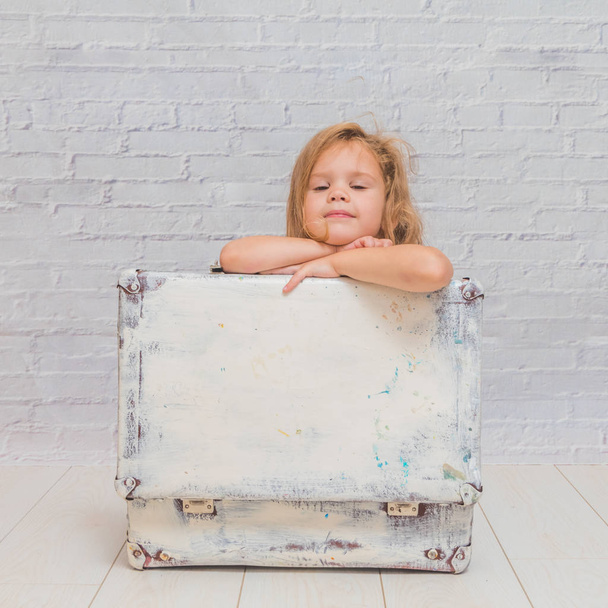 meisje, baby in jurk op witte bakstenen muur achtergrond met koffer - Foto, afbeelding