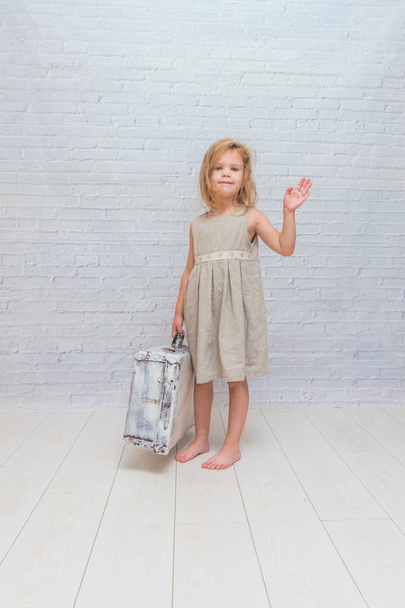 girl, baby in dress on white brick wall background with suitcase - Valokuva, kuva