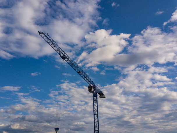 Een verhoogde bouw kraan tegen de blauwe lucht en de witte wolken op een zomerdag op het bouwterrein verhoogt de lading. - Foto, afbeelding