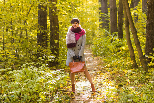 Φθινόπωρο, φύση και άνθρωποι έννοια - νεαρή όμορφη γυναίκα σε γκρι παλτό έχει ένα υπόλοιπο σε Φθινοπωρινό πάρκο - Φωτογραφία, εικόνα