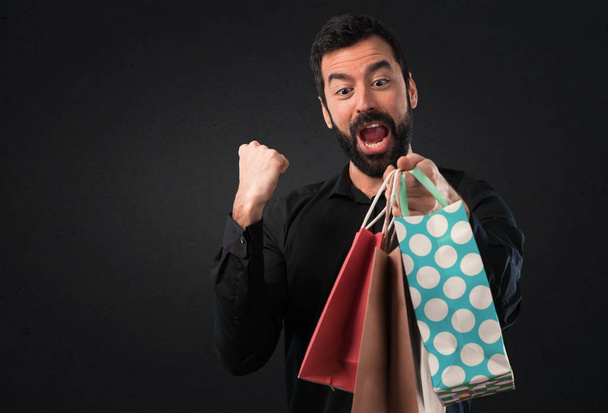 Handsome man with beard with shopping bag on black background - Photo, Image