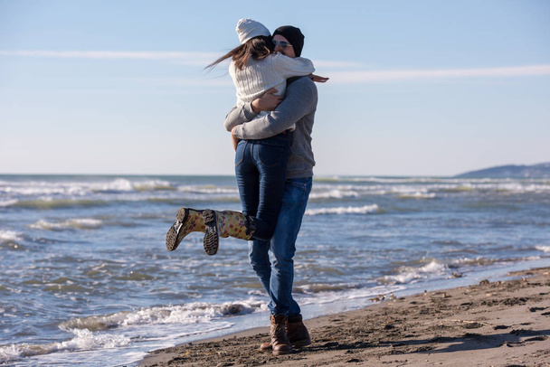 Young couple having fun walking and hugging on beach during autumn sunny day - Photo, Image