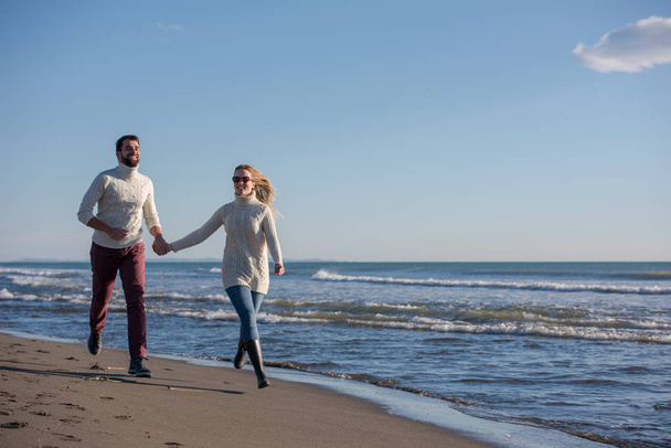 Young couple having fun walking and hugging on beach during autumn sunny day - Photo, Image