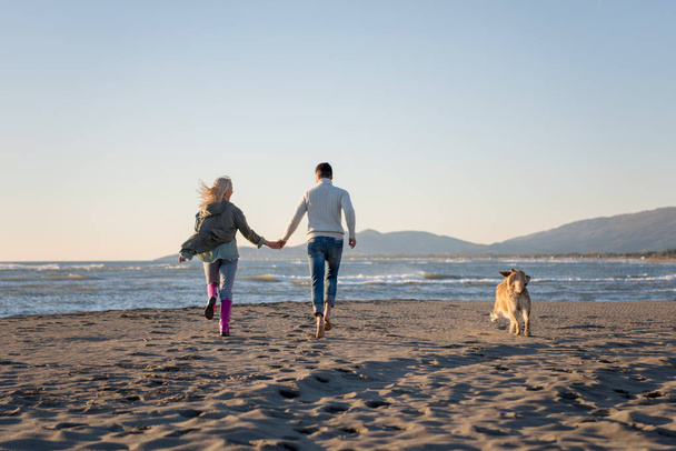 Пара бегущих по пляжу с собакой в день осени - Фото, изображение