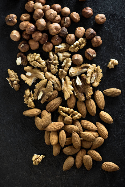 Organic Nuts. Various nuts (walnuts, hazelnuts, almonds)  on black stone background, top view, copy space. - Foto, Bild