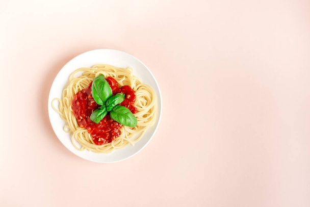 Spaghetti pasta bolognese on pink pastel background, top view. Plate of pasta dish with tomato sauce and basil on creative pink background. - Фото, изображение