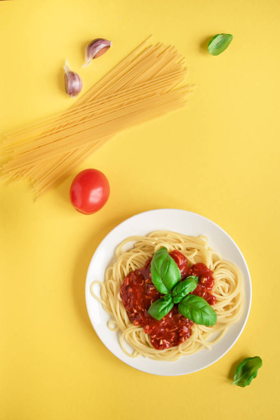 Spaghetti pasta bolognese and ingredients on yellow background, top view. Plate of pasta dish with tomato sauce and basil, creative yellow background. - Valokuva, kuva