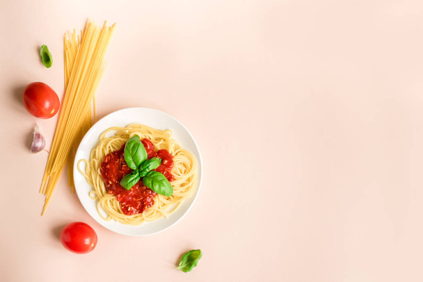 Spaghetti pasta bolognese and ingredients on pink background, top view. Plate of pasta dish with tomato sauce and basil, creative pastel background. - Photo, Image