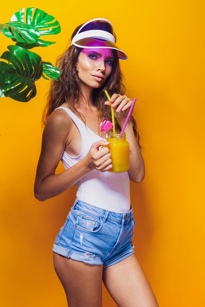 Sexy Woman in white swimsuit and blue jeans shorts, trendy visor holding beverage - Fotoğraf, Görsel