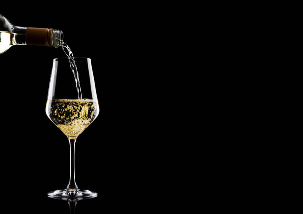 Pouring white wine from bottle to glass isolated on black background - Фото, изображение
