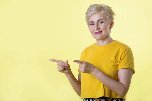 beautiful stylish woman with a short hairstyle on a yellow background with a gesture of hands - Valokuva, kuva