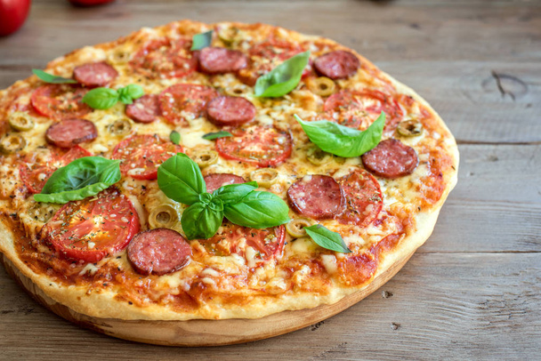 Italian Pizza with Tomatoes, Salami, green Olives, Cheese and Basil leaves on wooden table. Fresh Homemade Pizza, copy space. - 写真・画像
