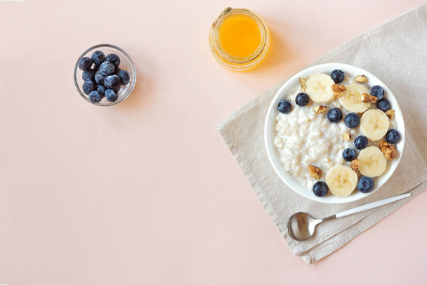 Oatmeal porridge with walnuts, blueberries and banana in bowl on pink pastel background - healthy organic breakfast, oats with fruits, honey and nuts - Zdjęcie, obraz