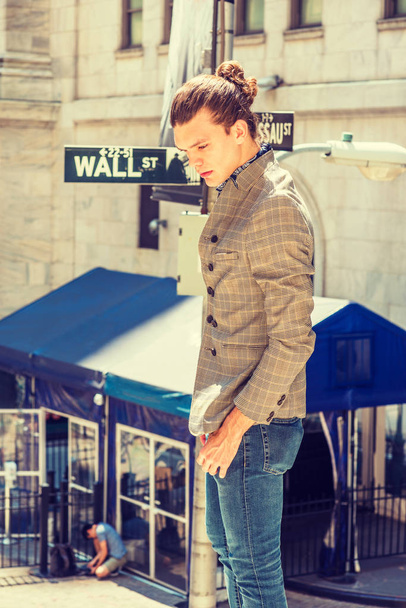 Deeply Serious Thinking On Wall Street in New York City. Young Hispanic American Man with hair bun, wearing brown patterned double breasted blazer, blue jeans, standing on street, looking down, thin - Photo, Image