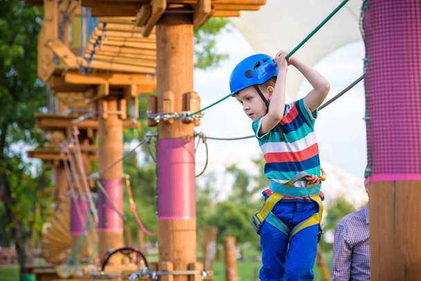 Little cute boy enjoying activity in a climbing adventure park on a summer sunny day. toddler climbing in a rope playground structure. Safe Climbing extreme sport with helmet and Carabiner. insurance - Photo, Image