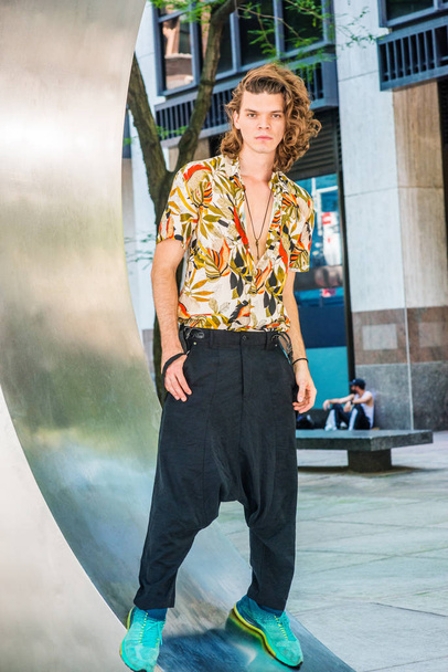 Portrait of Young American Artist with brown curly hair in New York, wearing colorful patterned short sleeve shirt, baggy loose pants with suspenders, patterned sneakers, hanging old key as necklac - Photo, Image
