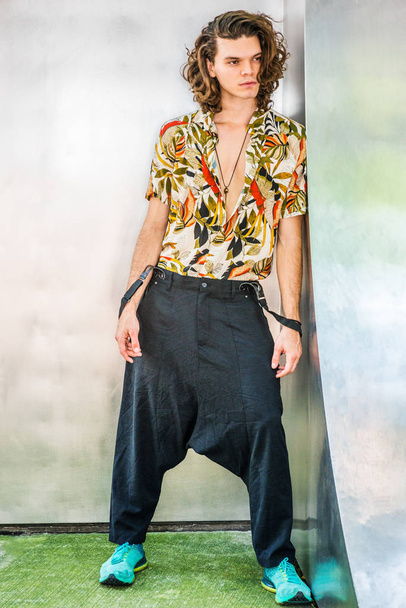 Hispanic-Amerikaans kunstenaar met bruin krullend haar in New York, dragen kleurrijke patroon shirt met korte mouwen, flodderige losse broek met bretels, patroon sneakers, opknoping oude sleutel als necklac - Foto, afbeelding